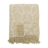 Pratello Throw in yellow, a woven fabric throw with a leafy floral pattern on a lighter ground, finished with fringed edges, folded on a plain white background.