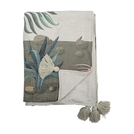 Peacock Throw in green, folded to show a printed garden scene with palm fronds, spiky leaves and stones, plus grey tassel trim, against a plain white background.