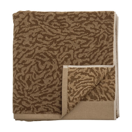 Kaysa Cotton Towel 140x70cm in brown, folded with a woven curling-branch pattern in light and dark tones and a plain beige border, shown on a white background.