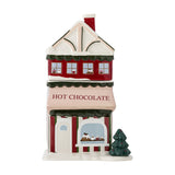 Gloria ceramic Christmas storage jar shaped as a red hot chocolate shop house with snow-topped roof, chimney, striped awning, and ceramic tree, 2500ml, on a white background.