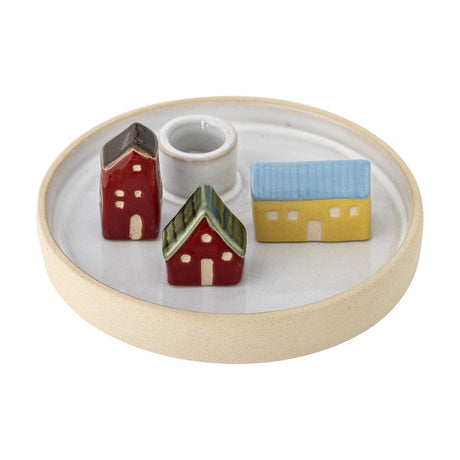 Coze round stoneware candle holder with a shallow rimmed base and central taper cup, surrounded by three glazed miniature houses in red, yellow, and blue, shown on a plain white background.