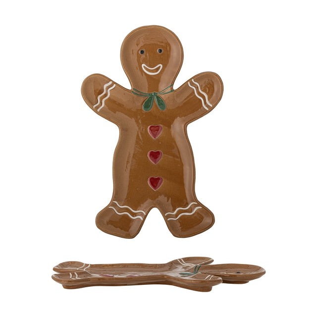 Glossy brown stoneware Christmas platter shaped like a smiling gingerbread man with a green bow, red hearts, and white icing details, stacked with a matching pair on a white background.