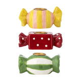 Set of three stoneware candle holders shaped like wrapped sweets with twisted ends in yellow-peach stripes, red polka dots, and green-white bands, each with a brass-tone candle cup.