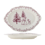 Oval stoneware Christmas platter with scalloped edge, pink painted scene of two deer among fir trees, and a pink floral vine border, shown from above and in profile.