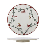 White stoneware lazy Susan with a fir garland and heart motifs linking a pig, candy cane, drum, horn and flag, on a low round base, plain white background.