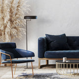 Rea 3 Light Dome Adjustable Swing Arm Floor Lamp in matt black, shown beside a navy sofa and armchair in a living room setting.