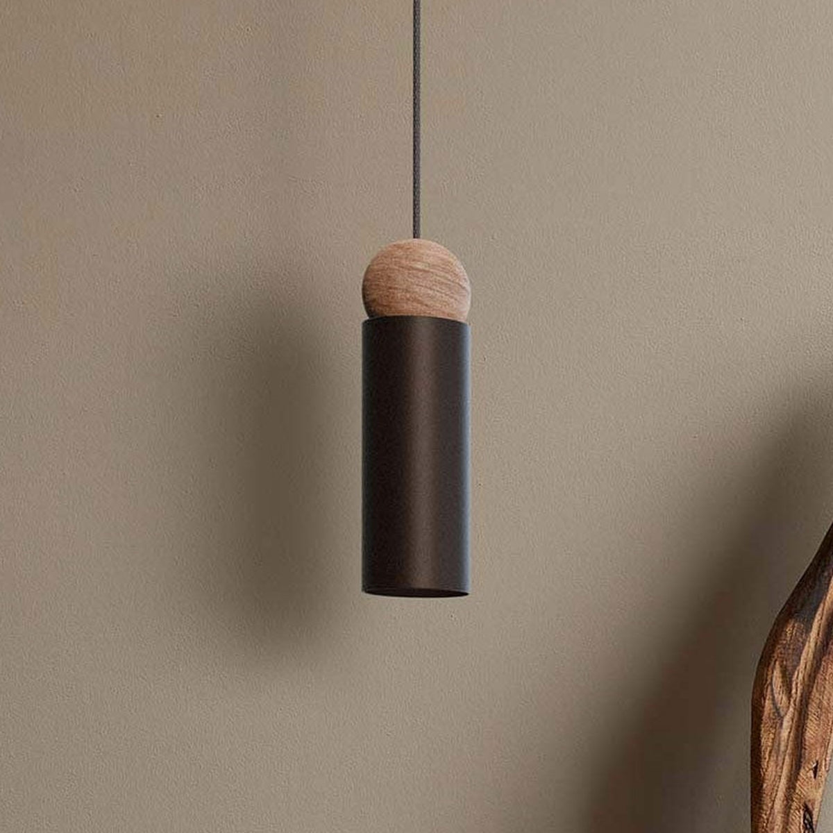 Rocio Wood Pendant Light in matt black, slim cylindrical metal shade topped with a round ash wood ball, hung on a textile cable against a plain neutral wall.