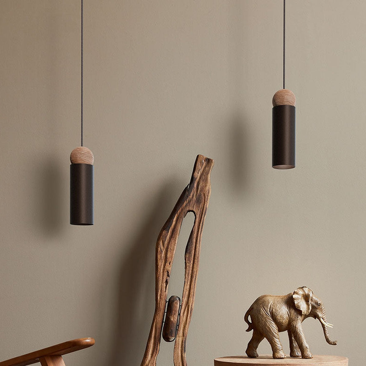Rocio Wood Pendant Light in matt black, slim cylindrical tube with an ash wood ball top, shown in pairs on textile cables above a wooden carving and elephant decor.