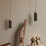Rocio Wood Pendant Light in matt black, slim cylindrical tube with an ash wood ball top, shown in pairs on textile cables above a wooden carving and elephant decor.