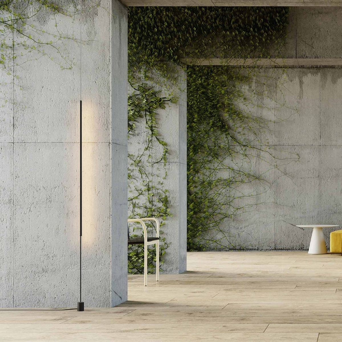 René LED Floor Lamp in matt black, a slim vertical light bar on a cylindrical base, shown against concrete walls in a plant-covered interior.