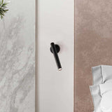 Rui LED adjustable wall light in matt black, slim cylindrical tube on round wall plate, mounted between marble and suede wall panels in a bedroom setting.