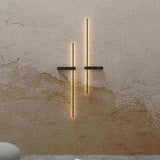Rut LED Linear Wall Light in matt black, two vertical bars with horizontal mounting brackets, mounted on a textured plaster wall with warm ambient glow.