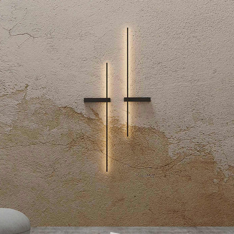 Rut LED Linear Wall Light in matt black, two vertical bars with horizontal mounting brackets, mounted on a textured plaster wall with warm ambient glow.