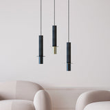 Rita Disc Pendant lights in black concrete with cylindrical columns, iron heads and flat discs, shown in brass and black finishes above armchairs.