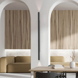 Rodi 2 Light Linear Wall Light in matt black iron, mounted between two archways in a living space with wood cabinetry and mustard sofas, casting light up and down the wall.