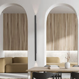 Rodi 2 Light Linear Wall Light in matt black iron, a slim vertical bar mounted between two arched wood-panelled alcoves, casting uplight and downlight in a dining area.