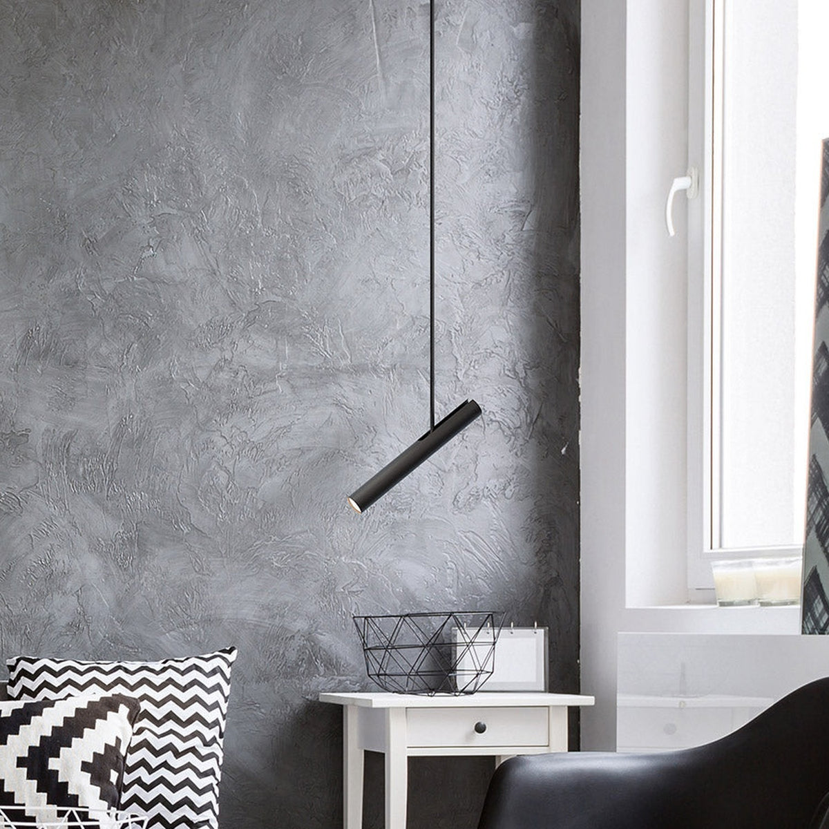 Rhoda Adjustable Linear Pendant Light in matt black iron, hung at an angle on a slim tube over a white bedside table in a grey-walled living space.