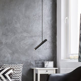 Rhoda Adjustable Linear Pendant Light in matt black iron, hung at an angle on a slim tube over a white bedside table in a grey-walled living space.