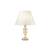 The Firenze Table Lamp - White boasts a timeless design featuring a white pleated lampshade accompanied by an elegant beige and gold base. When illuminated, it emits a warm glow that makes it a versatile piece suitable for any room.