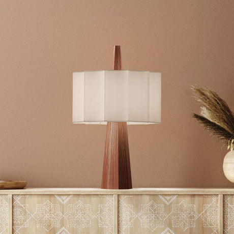 Rain Scalloped Fabric Table Lamp in chestnut, tapered faceted wood base with a central spire and white scalloped fabric shade, shown on a sideboard against a pink wall.