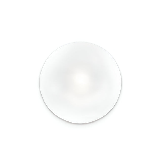 The Orlix Ceiling & Wall Light - White, 14cm features a smooth, clear glass lens centered on a white background. Its compact design casts a subtle shadow below, while the circular shape and transparency are enhanced by the light to create a soft gradient effect similar to white blown glass.