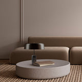 Romina Dome Mushroom Table Lamp with matt black dome shade on a dark marble cylindrical base, shown on a round stone coffee table beside a brown sofa.