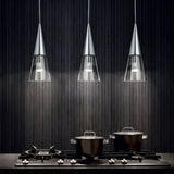 A modern kitchen scene with a black stovetop featuring three burners. Two pots with lids are on the stove. Above, three sleek Cone 1 Light Glass Pendants in silver with adjustable cable lengths illuminate the dark textured wall, creating a stylish, contemporary look.