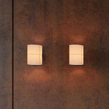 Rania Cylinder Fabric Wall Light in white cream with black base, two fitted on a textured rust-brown wall, glowing softly uplight and downlight.