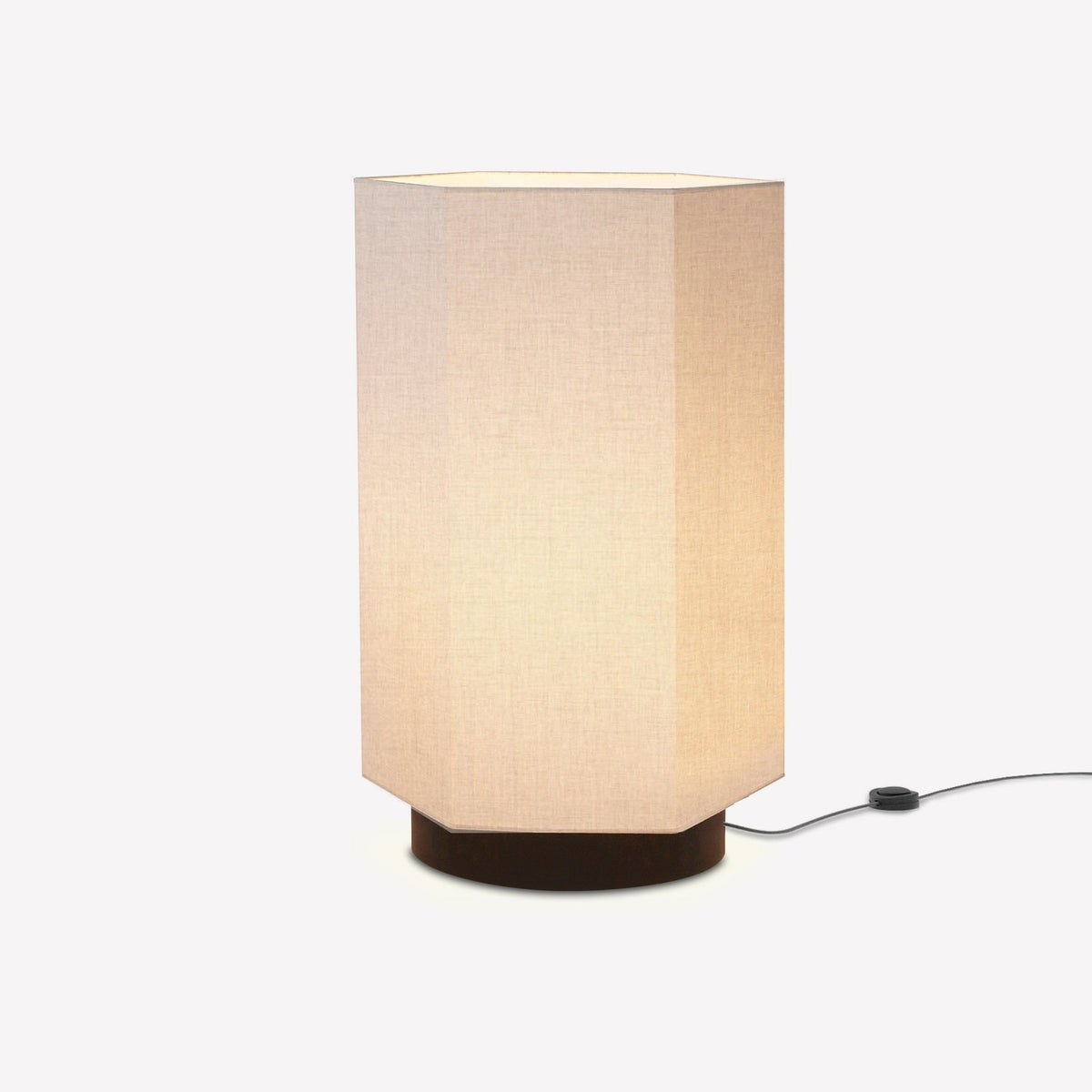 Roxi Fabric Floor Lamp with hexagonal natural fibre shade on a dark round base, glowing softly, shown on a plain white background.