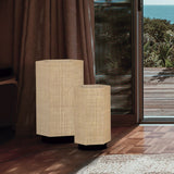 Roxi Fabric Floor Lamp in two sizes, hexagonal natural fibre shades on dark round bases, shown beside a curtained window with a sea view.