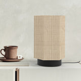 Roxi Fabric Table Lamp with hexagonal natural fibre shade and round black base, shown on a sideboard beside a cup and saucer against a neutral wall.