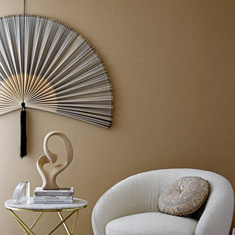 Jaime Bamboo Wall Decor in grey, a large fan-shaped wall art piece with fine bamboo canes and black tassel, hung above a boucle armchair and marble side table.