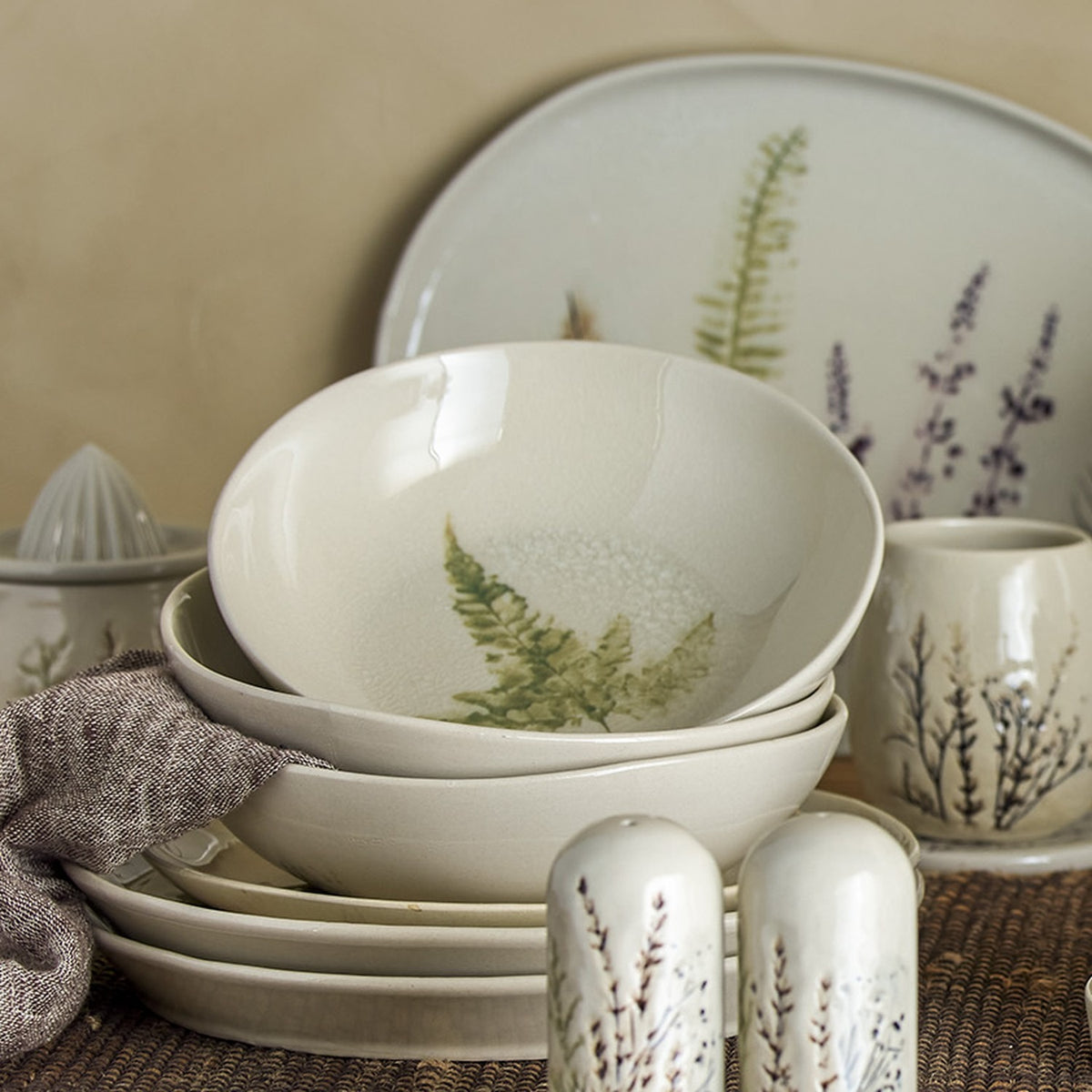 Bea Crackle Stoneware Deep Plate in cream with fern leaf motif, stacked among matching bowls, plates, and a jug with botanical patterns.
