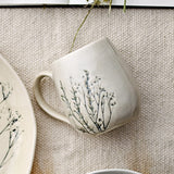 Bea Crackle Stoneware Mug 400ml in cream with crackle-glazed finish and botanical stem print, curved handle, shown beside a matching plate on a woven beige surface.