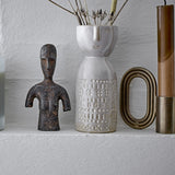 Embla Stoneware Vase 14.5cm in white, with a sculpted face near the rim and patterned dot and cross bands, shown on a shelf beside a dark figurine and candle.