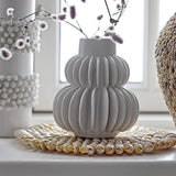 Halfdan Stoneware Vase 14cm in white with ribbed, tiered body and narrow neck, holding dried flowers on a windowsill beside textured hobnail vases.