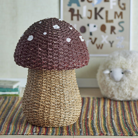 Corintha Mushroom Seagrass Basket with Lid in brown, domed spotted cap and woven stem, shown as nursery storage beside a plush sheep and alphabet print.