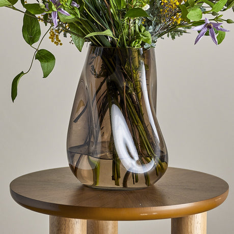 Ingolf Glass Vase 26cm in brown with a twisted, pinched body, holding a wildflower bouquet on a round wooden side table.