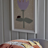 Numa Wooden Framed Print in multi, shown on a nursery wall above a patterned cushion, with a pale purple flower, green leaves and a ladybird on a spotted beige background.
