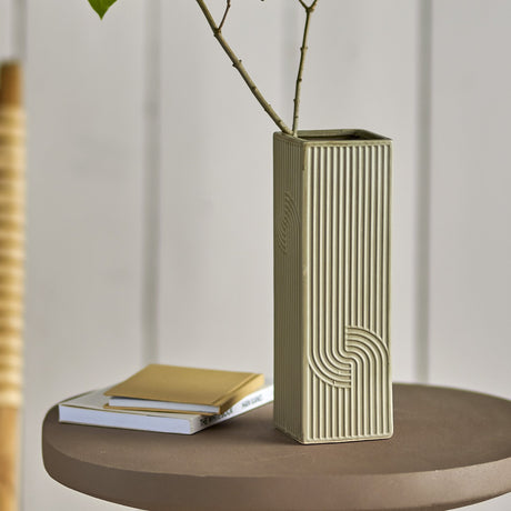 Heeira Square Stoneware Vase 26cm in beige with ribbed sides and interlocking arc detail, shown with a branch on a round table beside stacked books.