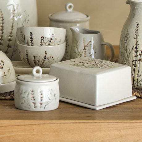 Bea Crackle Stoneware Butter Dish in cream with a floral motif and crackle glaze lid, shown among matching stoneware bowls, jugs, and jars with the same botanical design.