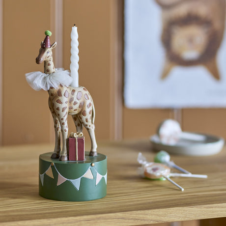 Flor Resin Candle Holder 25cm, a multicoloured giraffe-shaped candle holder in a party hat and ruff on a green bunting-painted drum base, shown on a wooden surface with a taper candle inserted.