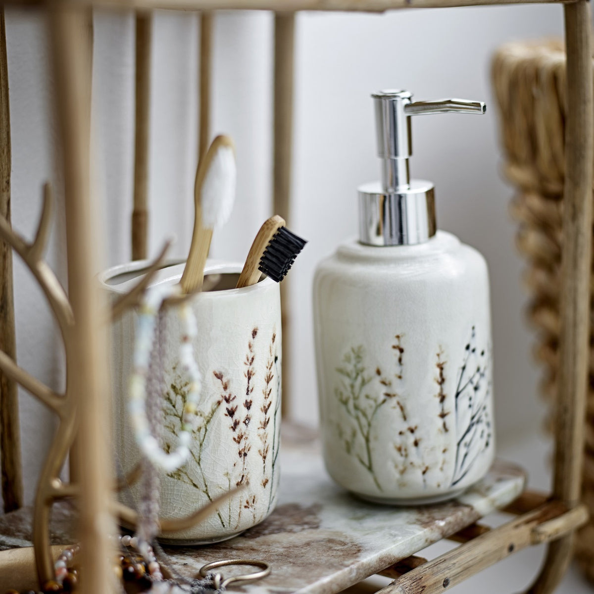 Bea Crackle Stoneware Soap Dispenser Set of 2 in beige, with chrome pump top and matching toothbrush cup, both featuring a crackle glaze and floral stem design, shown on a shelf.