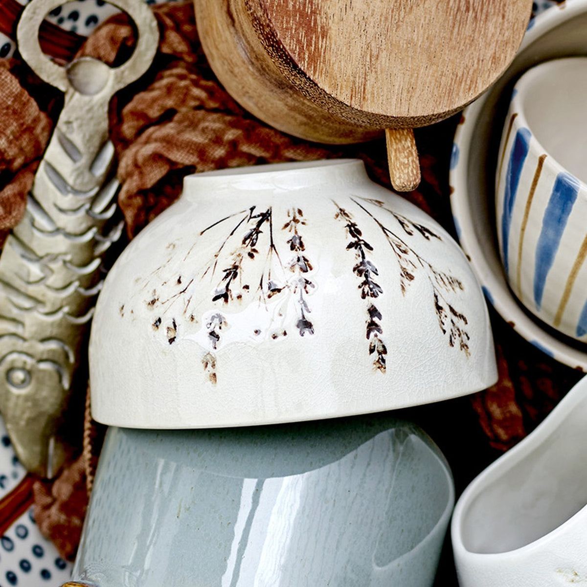 Bea Floral Stoneware Bowl 11.5cm in beige, shown upturned with fine sprig floral motif, glossy finish, among mixed ceramics and wooden items.