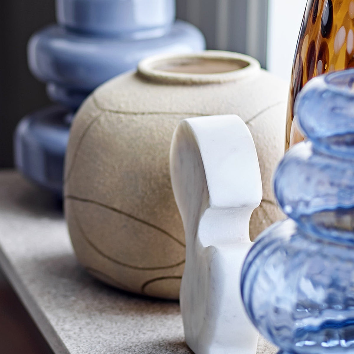 Niza Terracotta Vase 16.5cm in Natural, a rounded vase with narrow raised-rim neck and fine looping line pattern, shown with marble and glass decor pieces on a shelf.
