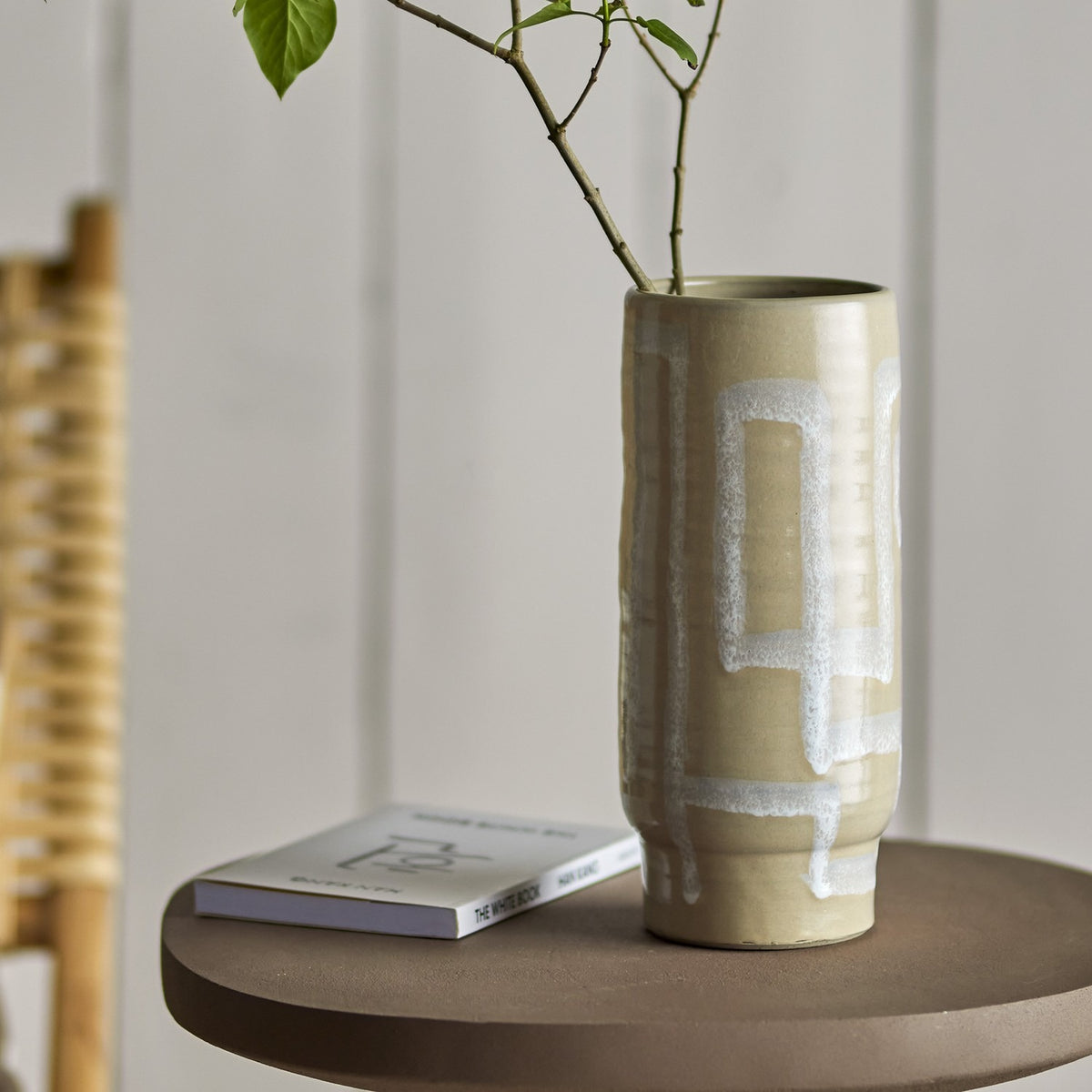Vefa Terracotta Vase in natural tone, 28.5cm tall cylindrical form with pale speckled glaze in looped band patterns, shown on a side table holding a leafy branch.