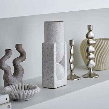 Salome Stoneware Vase 34cm in white, with a tall cylindrical neck rising from a rectangular base, shown on a shelf among candlesticks and decorative objects.