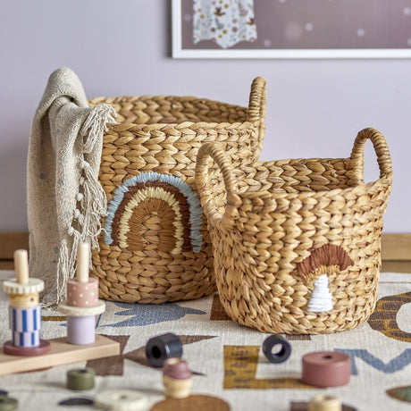 Agnes Water Hyacinth Baskets Set of 2 in beige, round woven storage baskets with handles, one stitched with a rainbow motif and the smaller with a mushroom design, shown in a nursery setting.