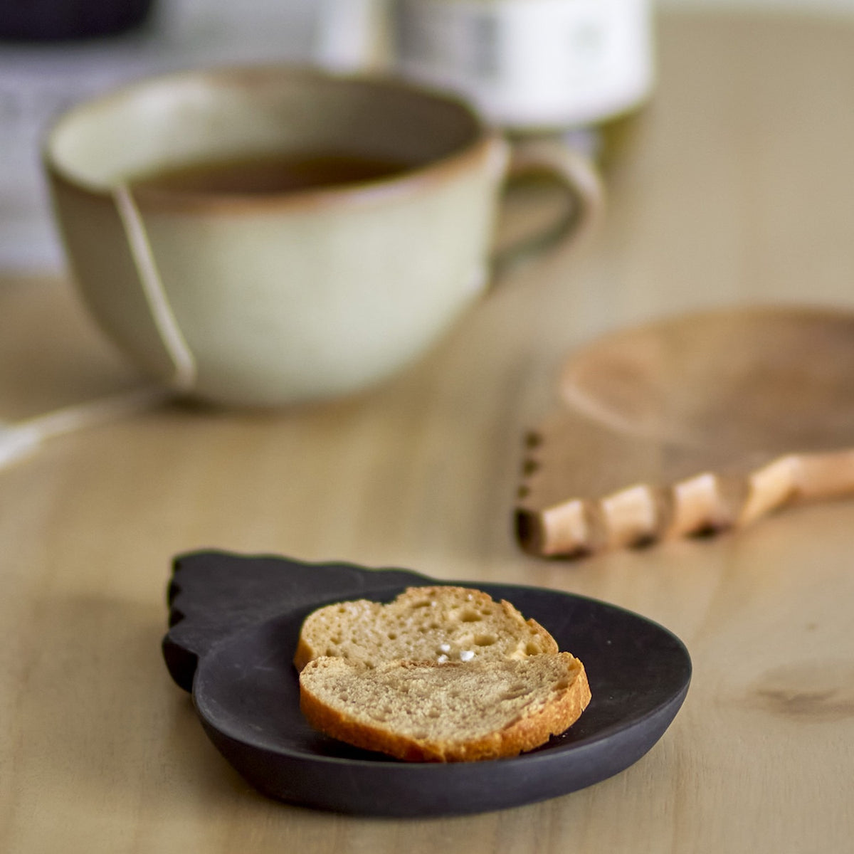 Tiara wooden bowl from the set of 2, a shallow acacia wood dish with scalloped tab handle, shown holding a slice of bread beside a cup of tea on a wooden table.