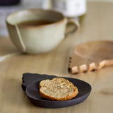 Tiara wooden bowl from the set of 2, a shallow acacia wood dish with scalloped tab handle, shown holding a slice of bread beside a cup of tea on a wooden table.